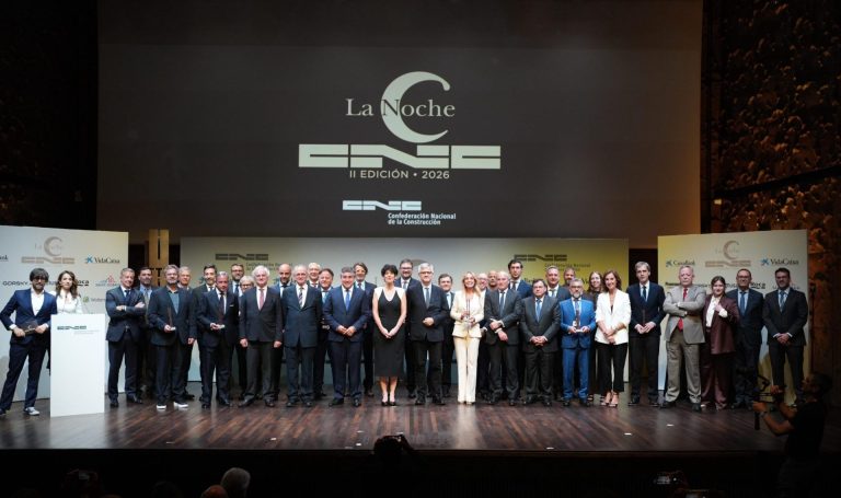 Group of professionals in formal attire posing on a stage at an awards ceremony, with a large screen displaying 'La Noche' and logos in the background.